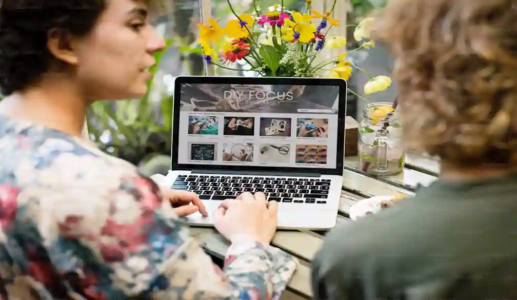 Two people sitting at an outdoor cafe table collaborating over a laptop screen showing a website layout, representing personalized digital marketing consulting.